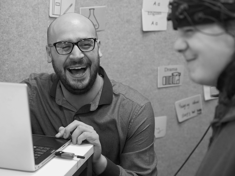Dr Horia Maior laughing with a participant wearing a scientific brain scanner, who is making a funny face while thinking harder.